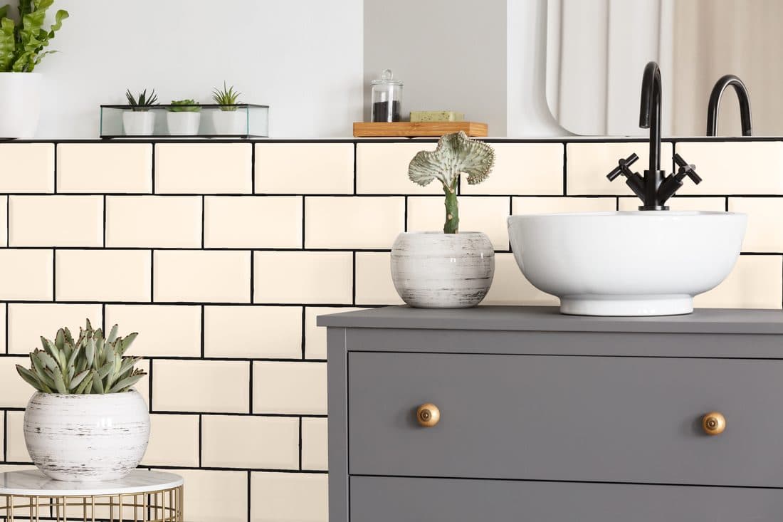 A neutral bathroom with cream tile and a painted dresser